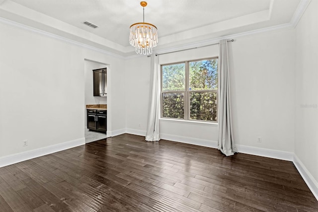 empty room featuring an inviting chandelier, a raised ceiling, dark hardwood / wood-style floors, and ornamental molding