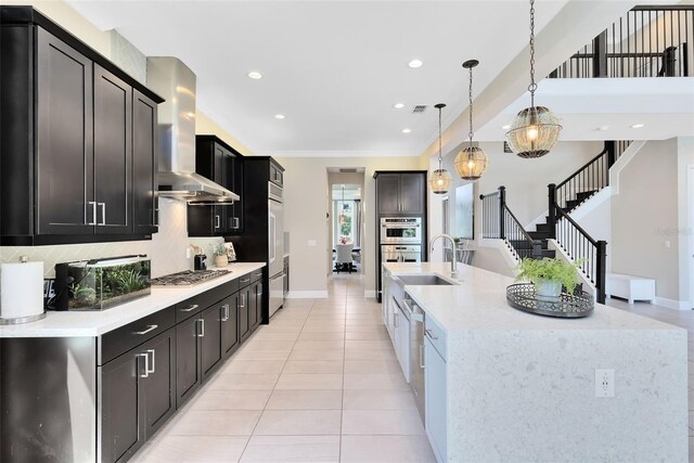 kitchen featuring a spacious island, wall chimney exhaust hood, sink, hanging light fixtures, and appliances with stainless steel finishes