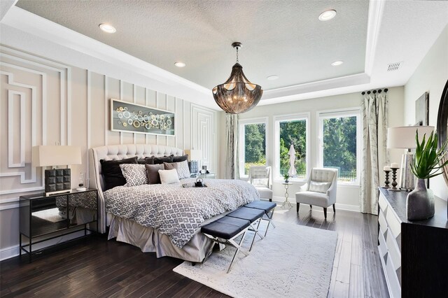 bedroom featuring dark hardwood / wood-style flooring, a tray ceiling, a chandelier, and a textured ceiling