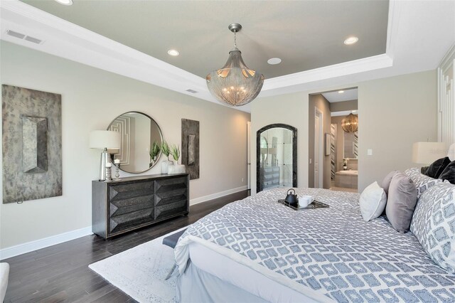 bedroom featuring dark wood-type flooring, ensuite bathroom, crown molding, a chandelier, and a raised ceiling