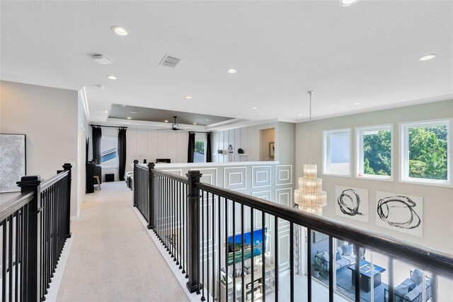 hall with crown molding, a raised ceiling, a chandelier, and light carpet