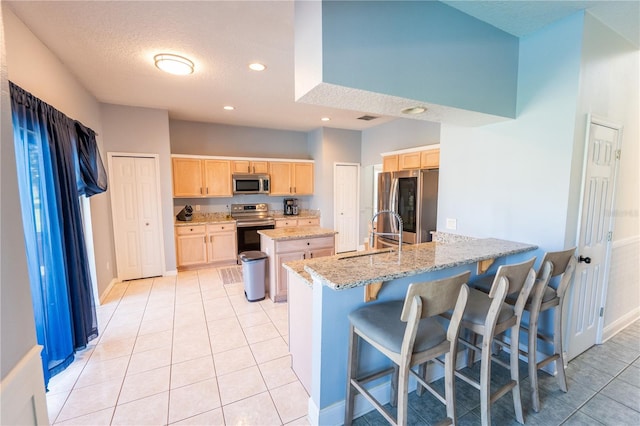 kitchen featuring light stone countertops, a center island, a kitchen breakfast bar, light brown cabinetry, and appliances with stainless steel finishes