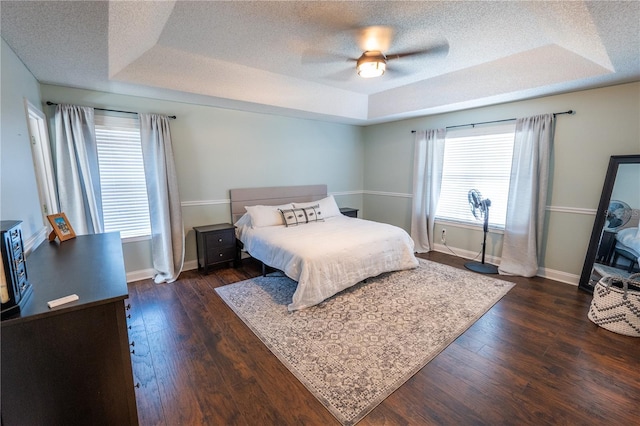 bedroom featuring a tray ceiling, multiple windows, ceiling fan, and dark hardwood / wood-style floors