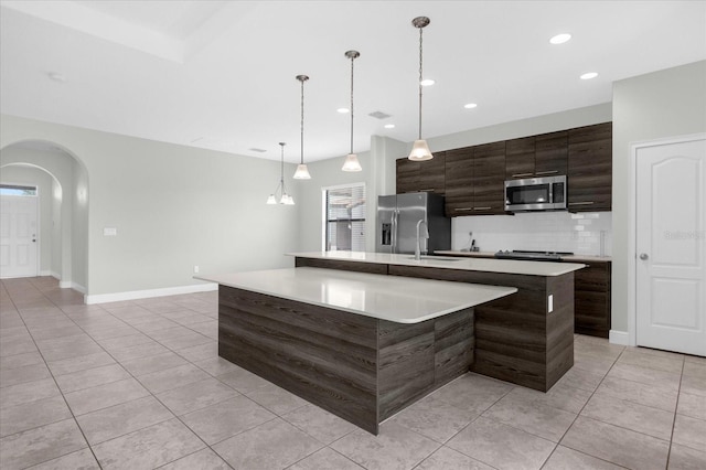 kitchen featuring hanging light fixtures, light tile patterned floors, an island with sink, appliances with stainless steel finishes, and dark brown cabinets