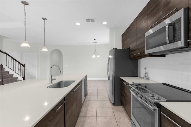 kitchen featuring pendant lighting, backsplash, sink, light tile patterned floors, and stainless steel appliances