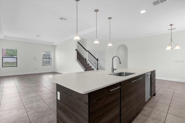 kitchen with dark brown cabinetry, sink, pendant lighting, light tile patterned floors, and a center island with sink