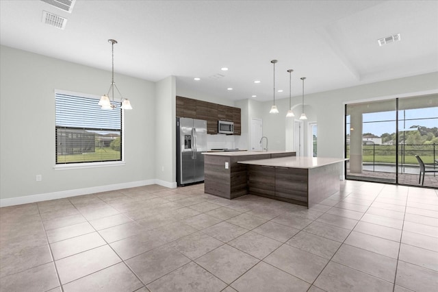 kitchen featuring appliances with stainless steel finishes, light tile patterned floors, dark brown cabinets, and an island with sink