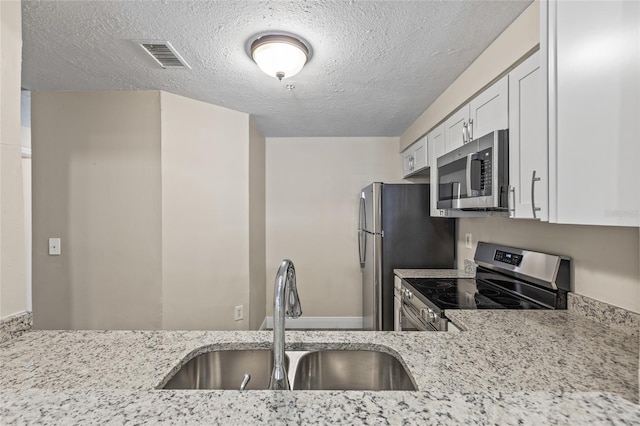 kitchen with appliances with stainless steel finishes, white cabinetry, sink, light stone countertops, and a textured ceiling