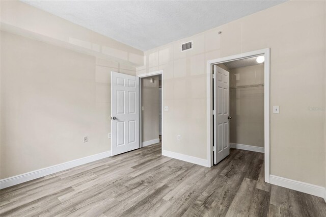 unfurnished bedroom featuring a walk in closet, wood-type flooring, a closet, and a textured ceiling