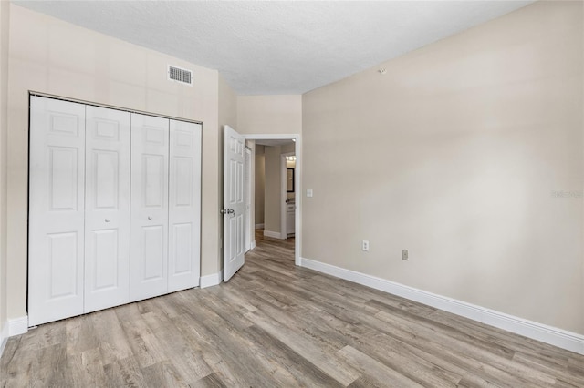 unfurnished bedroom with a textured ceiling, light hardwood / wood-style floors, and a closet