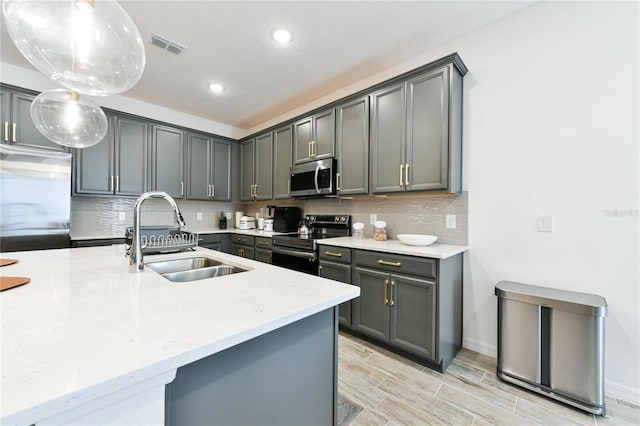 kitchen with sink, gray cabinetry, hanging light fixtures, stainless steel appliances, and light stone counters