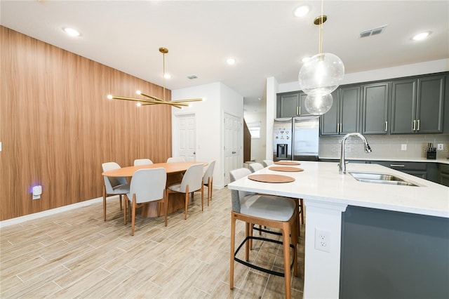 kitchen featuring hanging light fixtures, backsplash, sink, and stainless steel refrigerator with ice dispenser