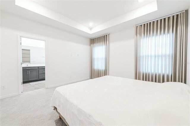 bedroom featuring light colored carpet, connected bathroom, and a tray ceiling