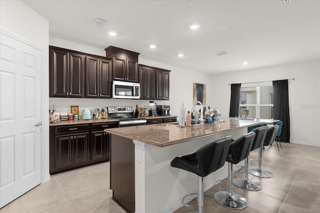 kitchen featuring stone countertops, a sink, a kitchen breakfast bar, appliances with stainless steel finishes, and an island with sink