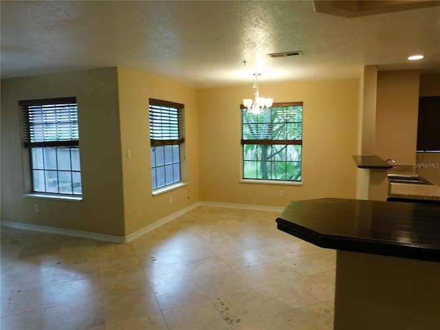 unfurnished dining area with a chandelier and a textured ceiling