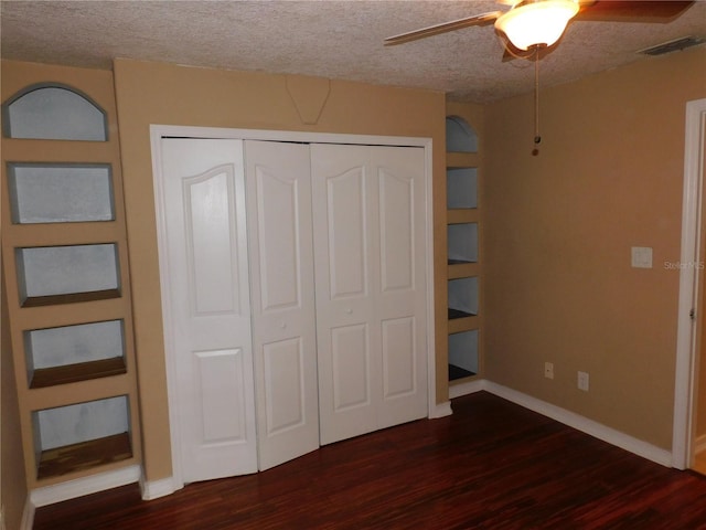 unfurnished bedroom featuring a textured ceiling, dark wood-type flooring, ceiling fan, and a closet