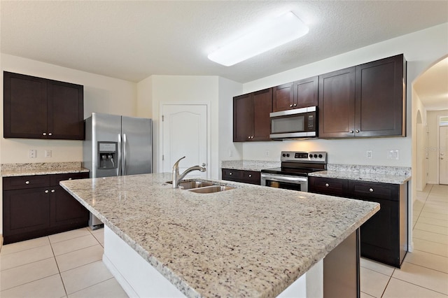 kitchen featuring stainless steel appliances, sink, light stone countertops, a center island with sink, and light tile patterned flooring