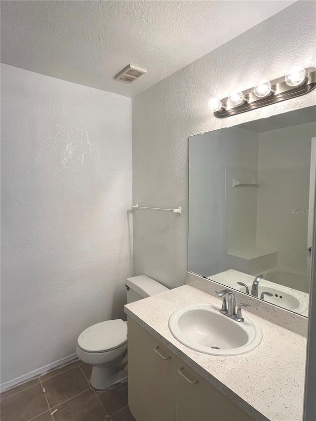 bathroom with tile patterned floors, vanity, a textured ceiling, and toilet