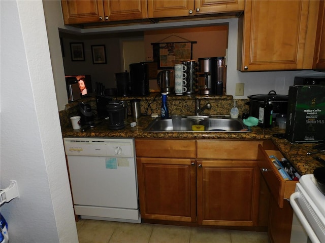 kitchen featuring sink, dishwasher, dark stone counters, and light tile patterned floors