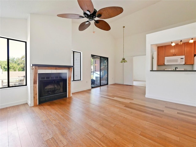 unfurnished living room featuring a fireplace, ceiling fan, light hardwood / wood-style floors, and high vaulted ceiling