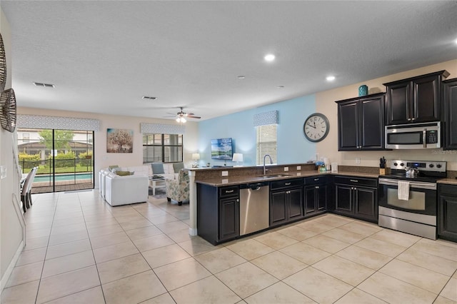 kitchen with a textured ceiling, appliances with stainless steel finishes, sink, kitchen peninsula, and light tile patterned floors