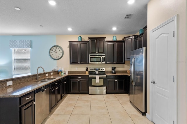 kitchen with stainless steel appliances, dark stone counters, sink, kitchen peninsula, and light tile patterned floors