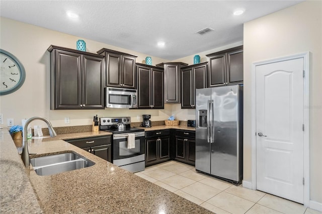 kitchen featuring appliances with stainless steel finishes, sink, light tile patterned flooring, a textured ceiling, and dark brown cabinetry