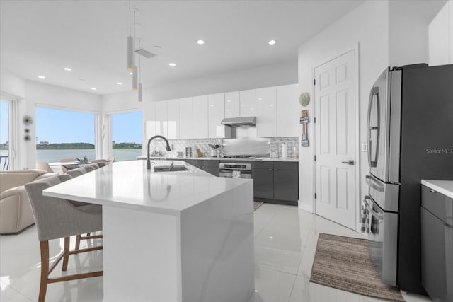 kitchen featuring a water view, sink, an island with sink, appliances with stainless steel finishes, and white cabinetry