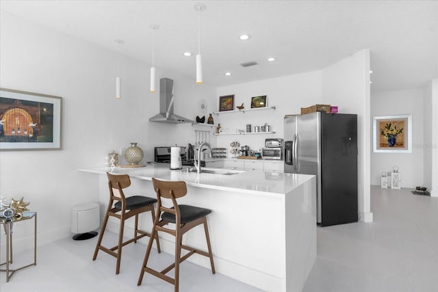 kitchen featuring stainless steel refrigerator with ice dispenser, sink, wall chimney range hood, decorative light fixtures, and white cabinetry