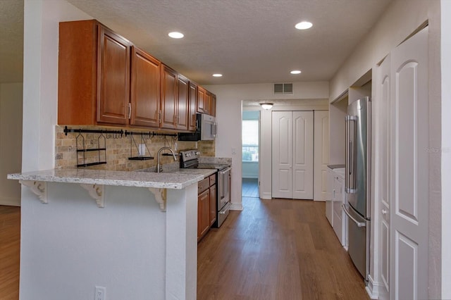 kitchen with kitchen peninsula, light hardwood / wood-style flooring, appliances with stainless steel finishes, tasteful backsplash, and a breakfast bar