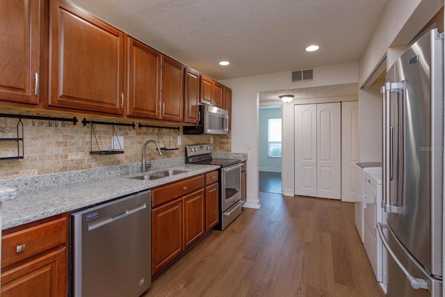 kitchen featuring sink, light wood-type flooring, backsplash, stainless steel appliances, and light stone counters