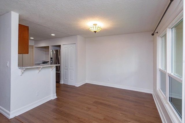 kitchen featuring high end refrigerator, kitchen peninsula, dark wood-type flooring, light stone counters, and a breakfast bar area