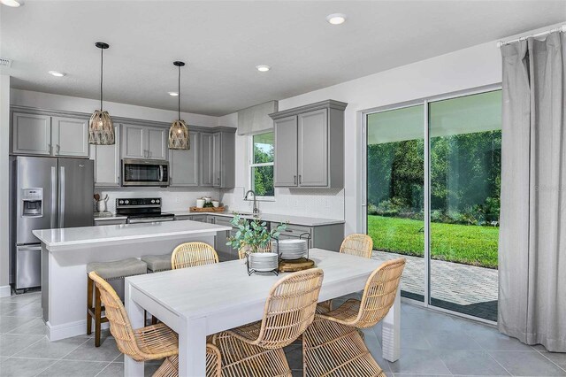 kitchen with stainless steel appliances, sink, pendant lighting, gray cabinets, and a kitchen island