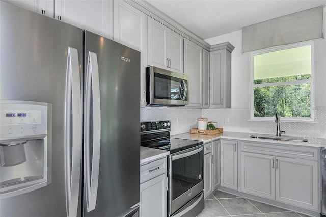 kitchen featuring sink, light stone counters, backsplash, light tile patterned floors, and appliances with stainless steel finishes