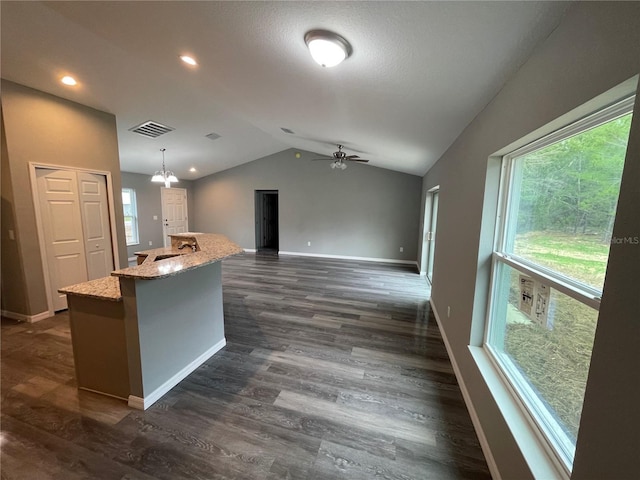 kitchen with pendant lighting, a kitchen island with sink, dark hardwood / wood-style floors, light stone counters, and vaulted ceiling