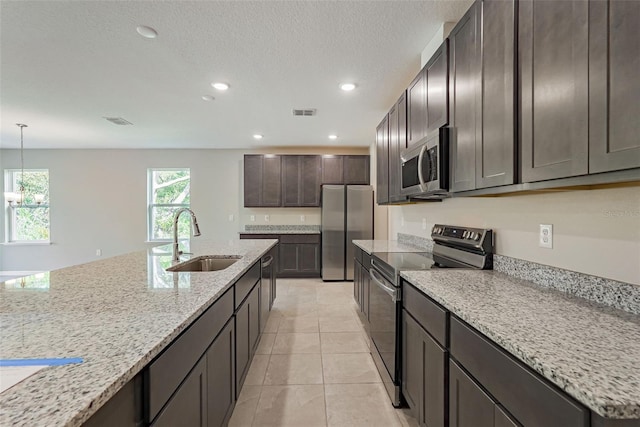 kitchen featuring sink, appliances with stainless steel finishes, dark brown cabinetry, light stone countertops, and decorative light fixtures