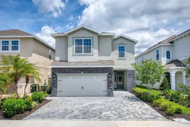 view of front of property featuring an attached garage, stone siding, decorative driveway, and stucco siding