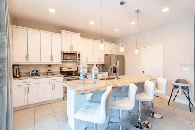 kitchen with appliances with stainless steel finishes, sink, pendant lighting, a kitchen island with sink, and white cabinetry