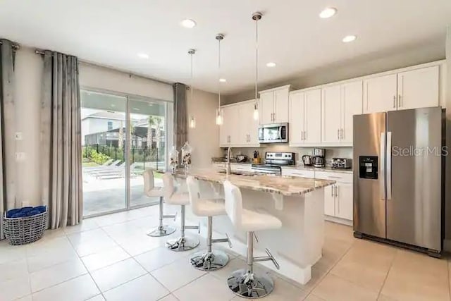 kitchen featuring light tile patterned flooring, white cabinets, an island with sink, stainless steel appliances, and pendant lighting