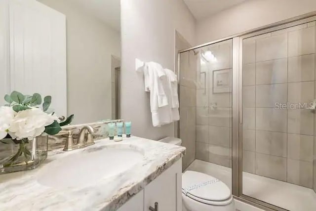 bathroom with a shower with shower door, vanity, and toilet