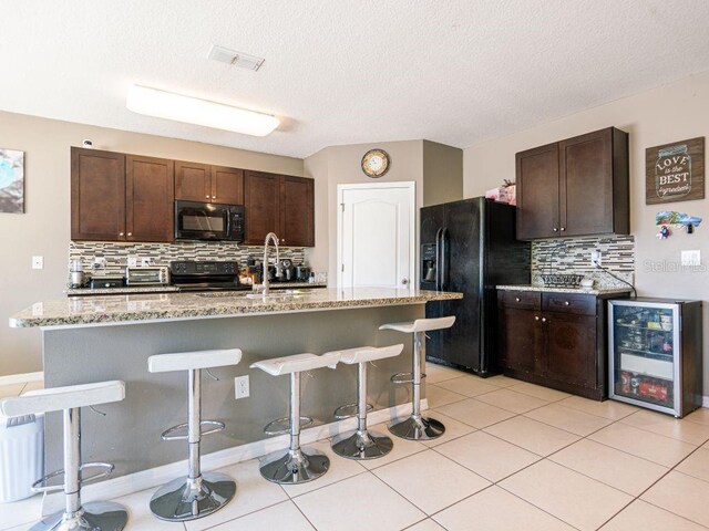 kitchen featuring tasteful backsplash, a kitchen island with sink, wine cooler, a kitchen bar, and black appliances