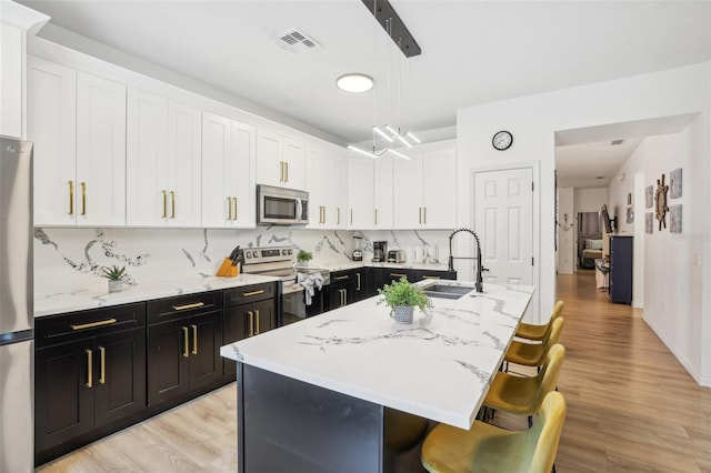 kitchen with pendant lighting, a breakfast bar area, stainless steel appliances, tasteful backsplash, and an island with sink