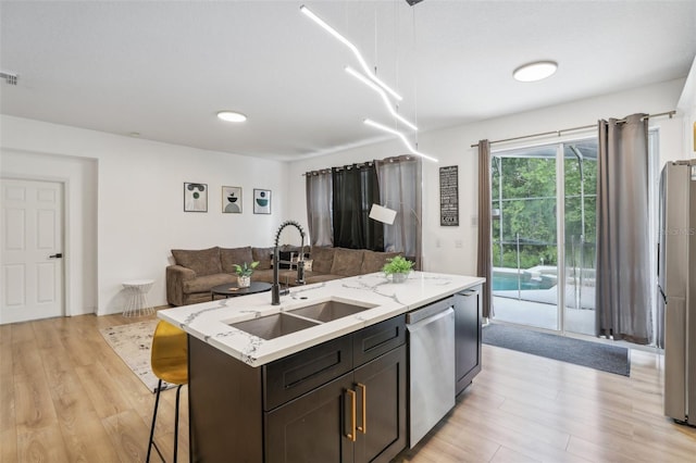 kitchen featuring sink, hanging light fixtures, a kitchen island with sink, light stone counters, and stainless steel appliances