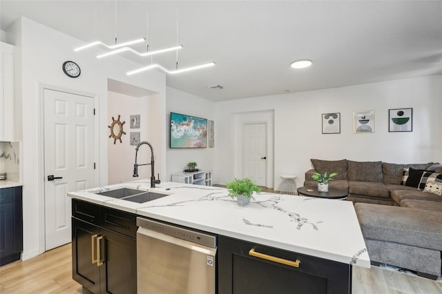 kitchen featuring sink, dishwasher, light hardwood / wood-style floors, an island with sink, and light stone countertops