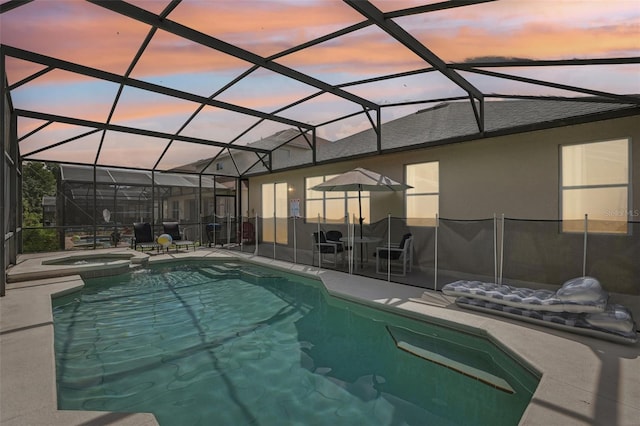 pool at dusk with a patio area, glass enclosure, and an in ground hot tub