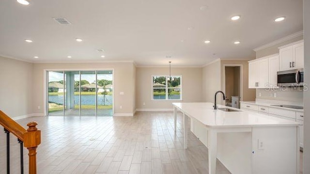 kitchen with ornamental molding, sink, white cabinets, and a center island with sink