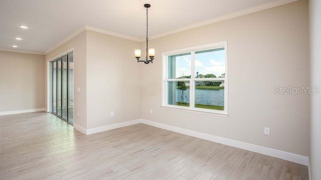 empty room featuring an inviting chandelier, a water view, light hardwood / wood-style flooring, and ornamental molding