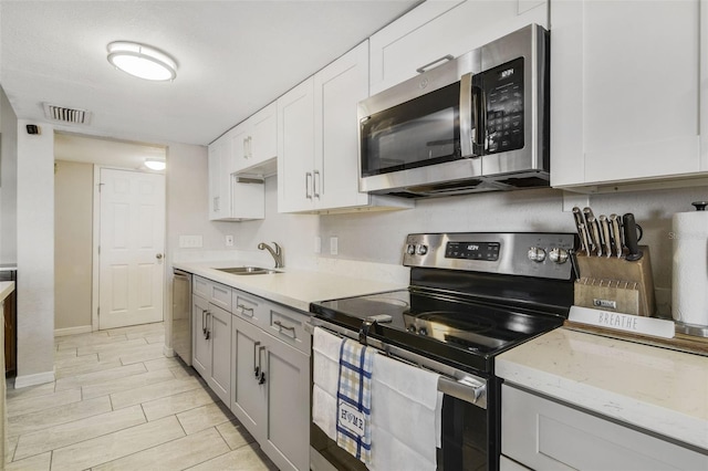 kitchen with light stone counters, light tile flooring, stainless steel appliances, gray cabinetry, and sink