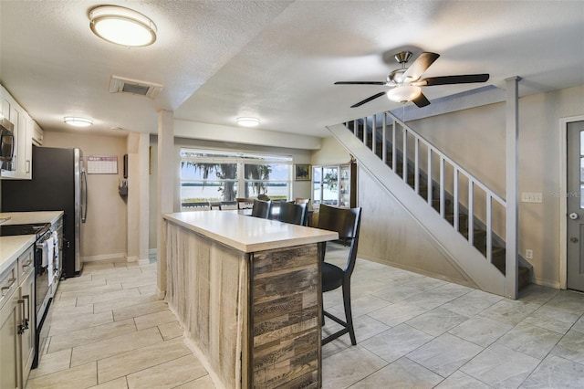 kitchen featuring white cabinetry, a textured ceiling, stainless steel appliances, ceiling fan, and light tile floors