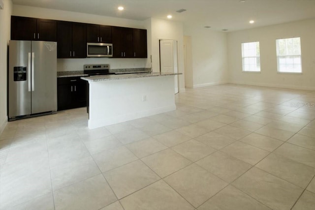 kitchen with a center island with sink, light stone counters, dark brown cabinetry, and stainless steel appliances